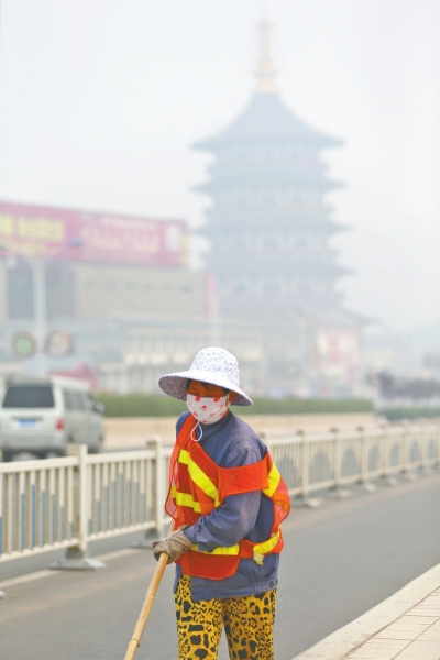 近日，在古都洛陽，環(huán)衛(wèi)工人身后的“天堂”被霧霾籠罩著。
