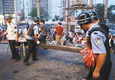 6月13日晚8點，朝陽路和青年路交叉口西側(cè)，一次聯(lián)合執(zhí)法行動中，輔警與協(xié)管抬走商戶的燒烤用具。新京報記者 尹亞飛 攝