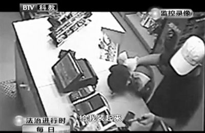 戴帽男子一手掐住加油站營業(yè)員，一手持發(fā)令槍指向另一營業(yè)員，要求“把錢給我裝起來”。