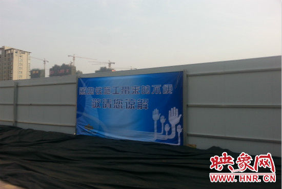 道路南側(cè)圍起了白色的圍擋，墻上標示著“因地鐵施工帶來的不便敬請您諒解”的提示牌。