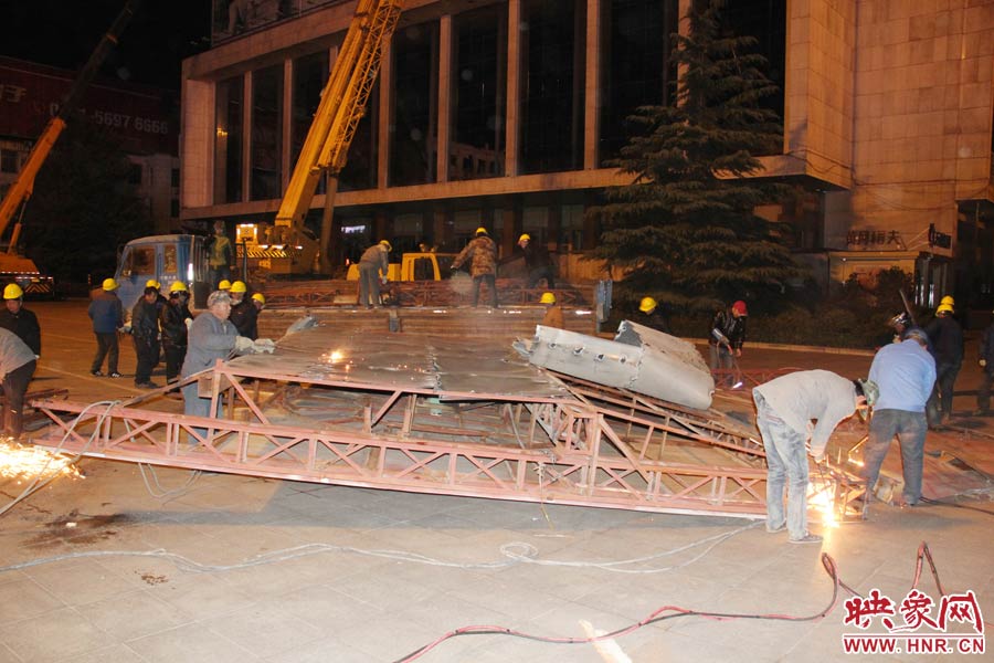 地面上的20多名工人對(duì)吊裝下的廣告牌進(jìn)行分割。