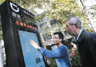 10月15日，滴滴工作人員（左）指導(dǎo)乘客使用“滴滴車(chē)站”的電子屏預(yù)約出租車(chē)。