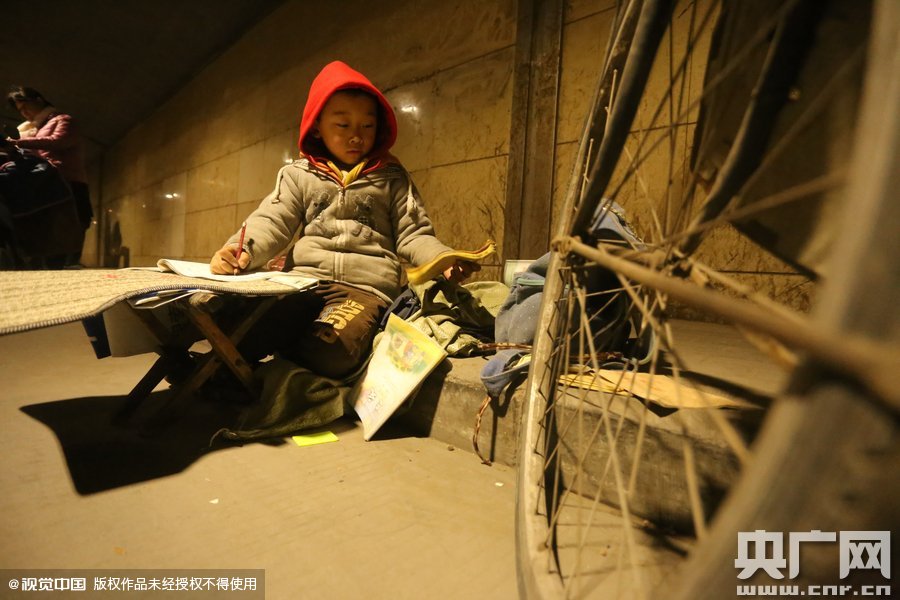 2015年11月8日晚，鄭州，7歲男孩涵洞橋下陪父母練攤，路邊燈下坐小馬扎上寫作業(yè)。