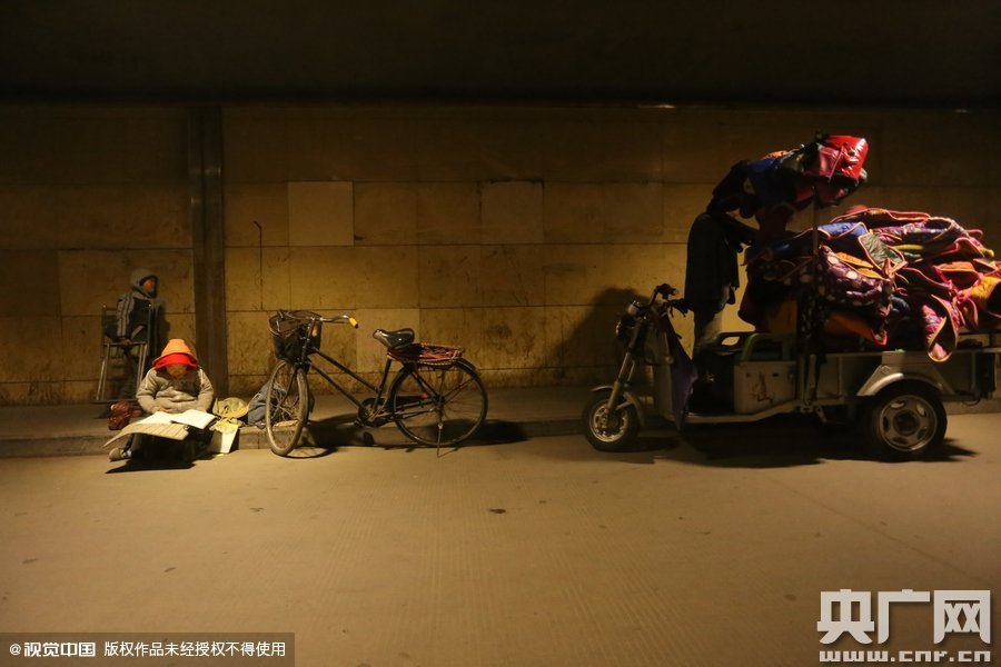 2015年11月8日晚，鄭州，7歲男孩涵洞橋下陪父母練攤，路邊燈下坐小馬扎上寫作業(yè)。