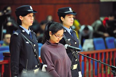 被告人盧梅低著頭，站在朝陽法院刑事審判庭的被告席上。